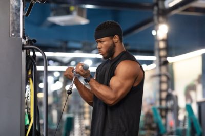 Concentrated black sportsman training muscles on block exerciser in gym, side view, copy space. Motivated african american bodybuilder having workout at modern gym, using peck deck machine