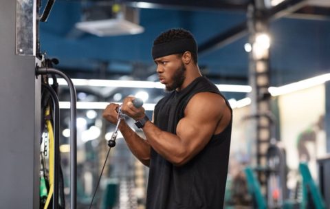 Concentrated black sportsman training muscles on block exerciser in gym, side view, copy space. Motivated african american bodybuilder having workout at modern gym, using peck deck machine